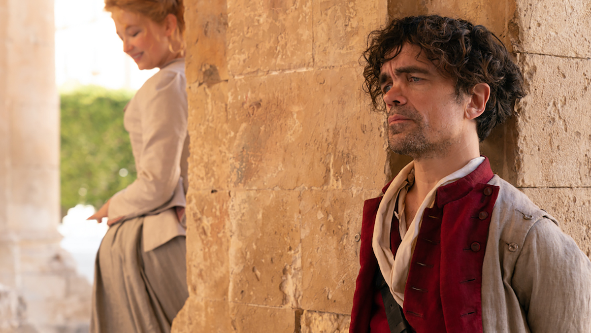 Peter Dinklage and Haley Bennett standing on opposite sides of the wall in Cyrano
