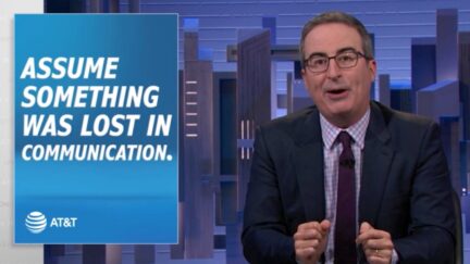 John Oliver speaks from his newsdesk during an episode of Last Week Tonight next to a graphic reading 