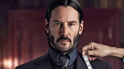 Keanu Reeves as John Wick looks into the camera as a tailor's hand holds a measuring tape to his collar