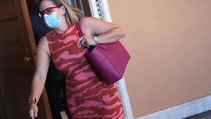 Kyrsten SInema dressed in a bright pink dress, rushes through the Capitol