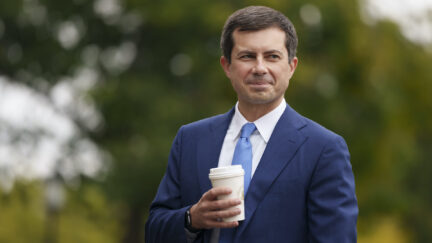 Pete Buttigieg smiles holding a cup of coffee outdoors