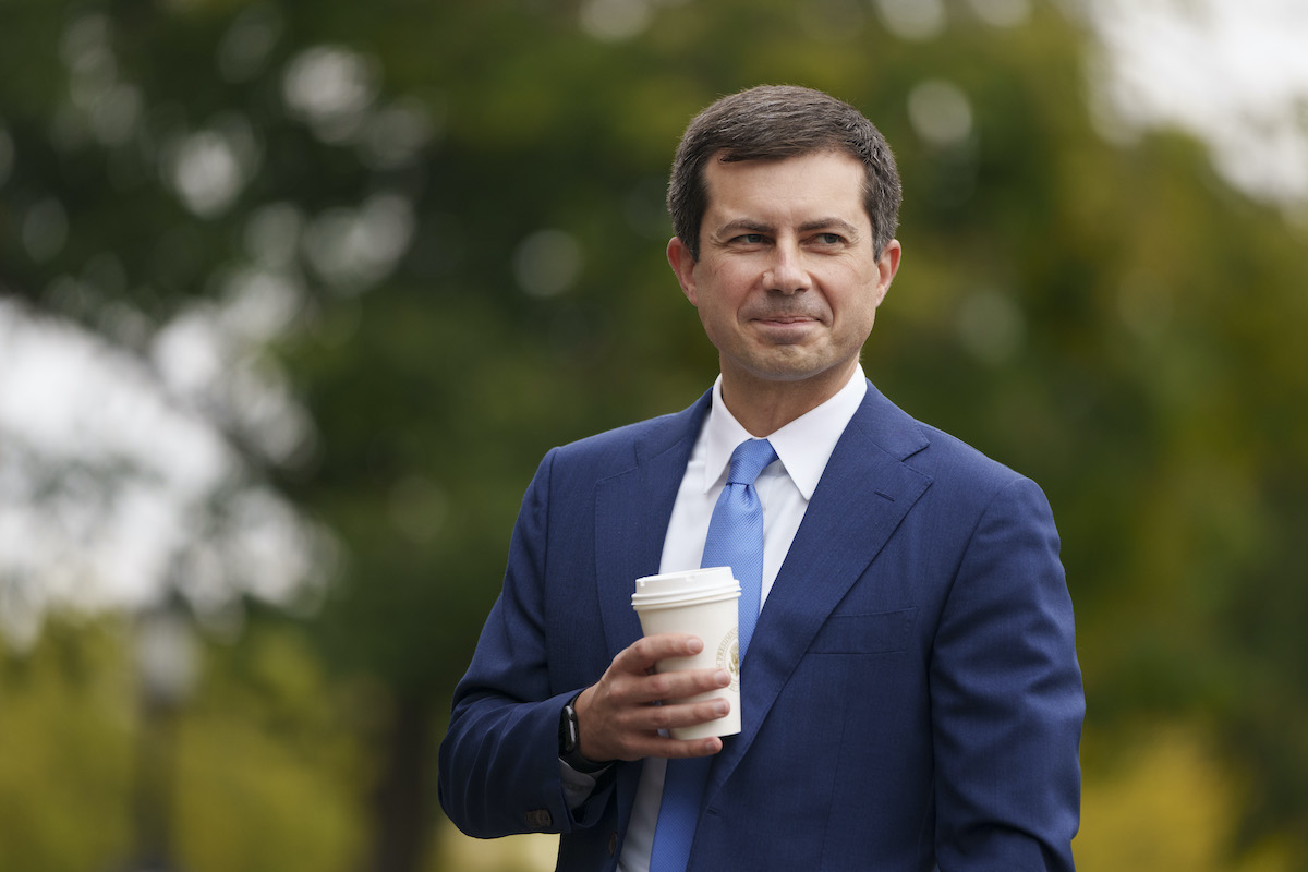 Pete Buttigieg smiles holding a cup of coffee outdoors
