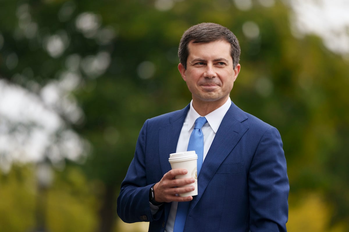 Pete Buttigieg smiles holding a cup of coffee outdoors