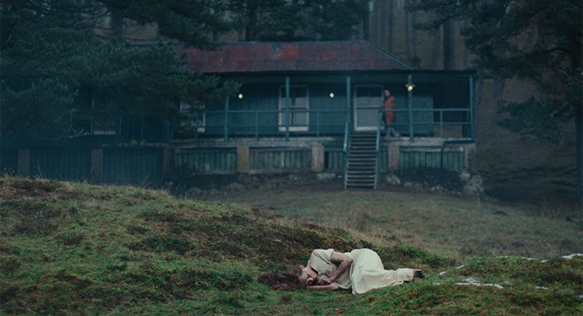 A woman in a white dress lies curled up in a field in the horror movie 'She Will'