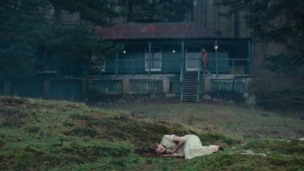 A woman in a white dress lies curled up in a field in the horror movie 'She Will'