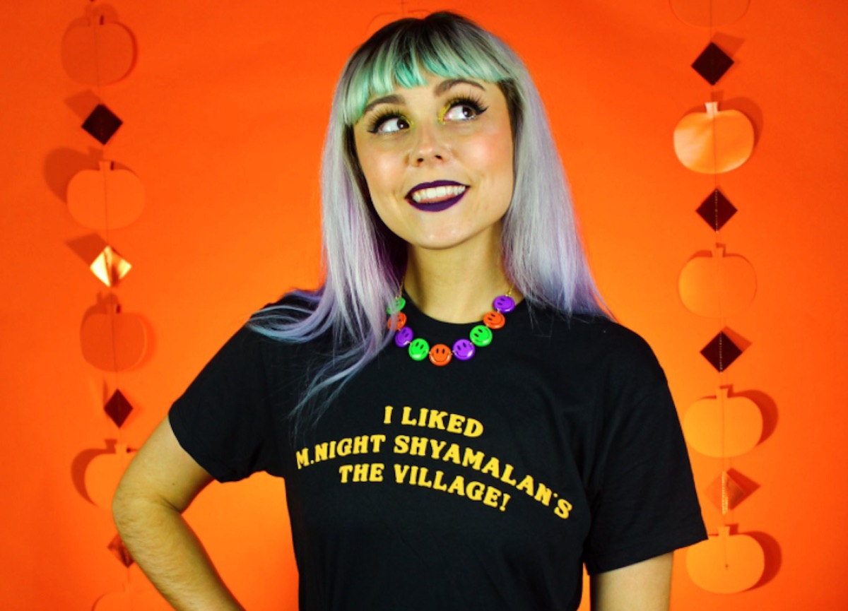 A woman wears a black Super Yaki t-shirt that says "I liked M. Night Shyamalan's The Village!"