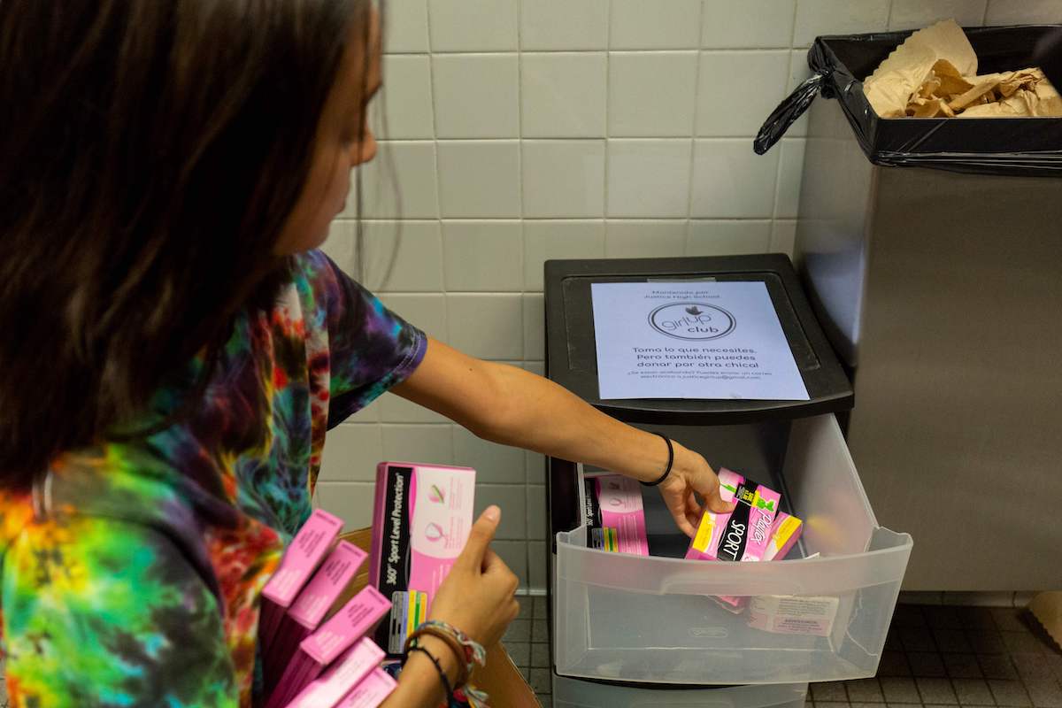 A student stocks a school bathroom with free pads and tampons