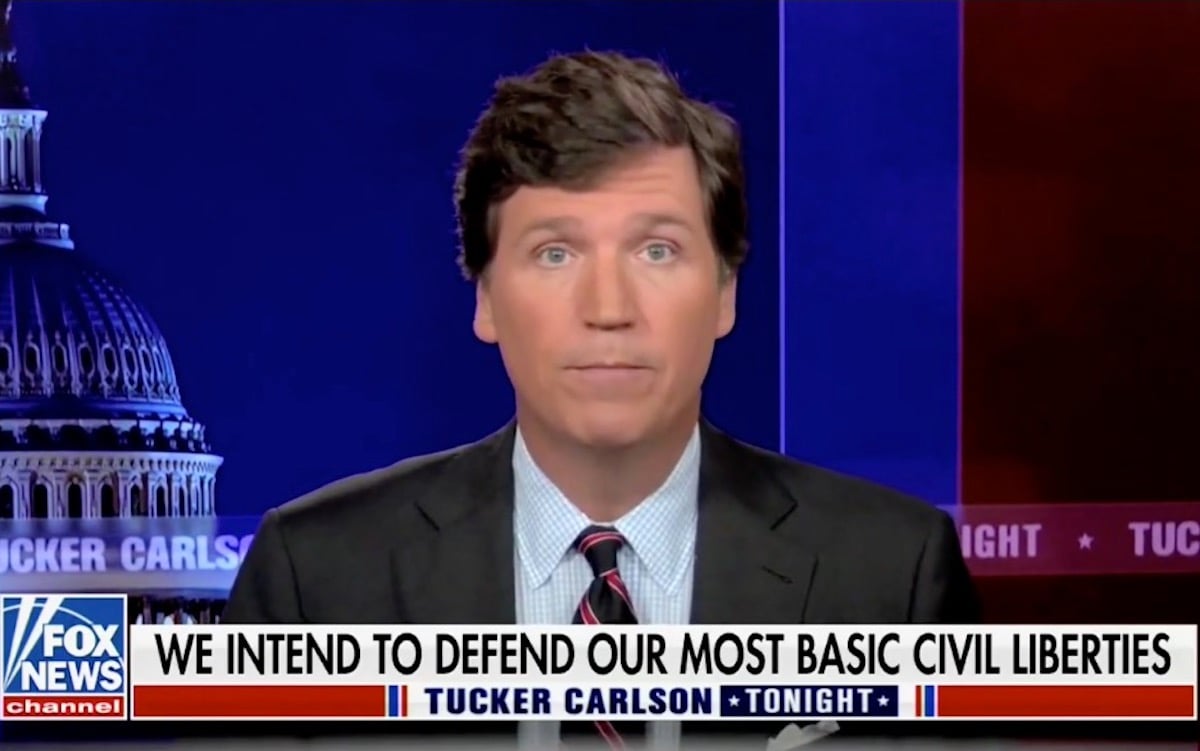 Tucker Carlson speaks during his Fox News show abover a chyron reading "We intend to defend our most basic civil liberties"