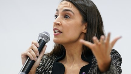Alexandria Ocasio-Cortez gestures while speaking into a microphone