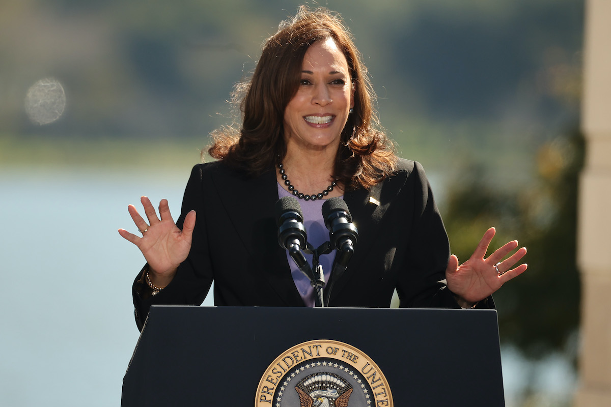 Kamala Harris speaks outdoors from a podium with the presidential seal on it.
