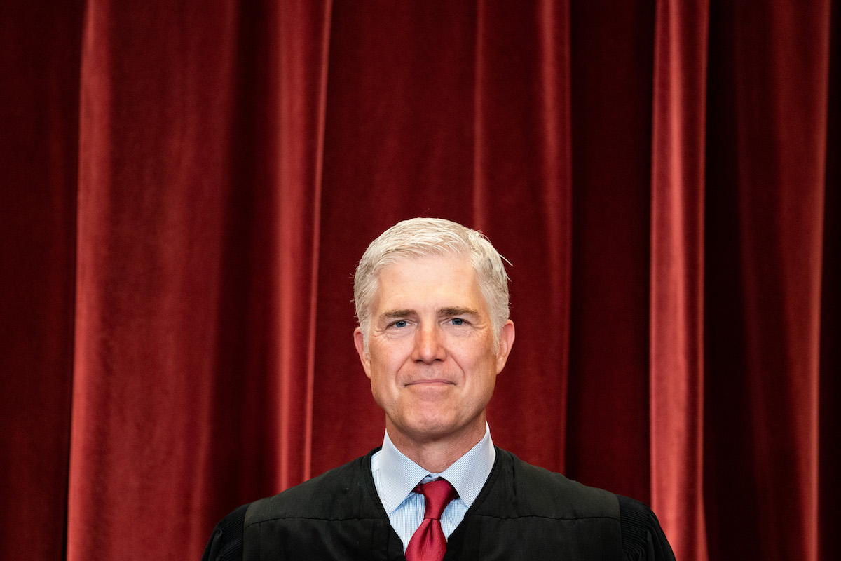 Neil Gorsuch smiles in his justice robe in front of a red curtain