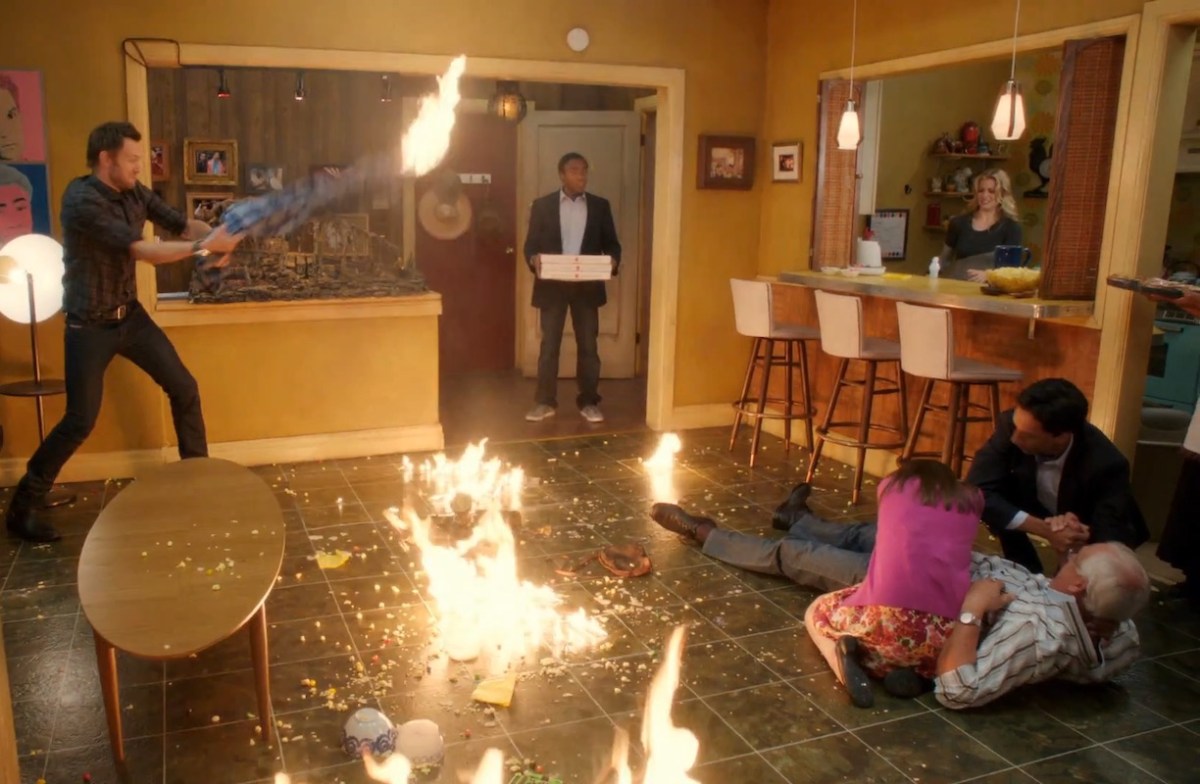 In a scene from Community, Troy stands holding pizzas while a fire breaks out in an apartment.