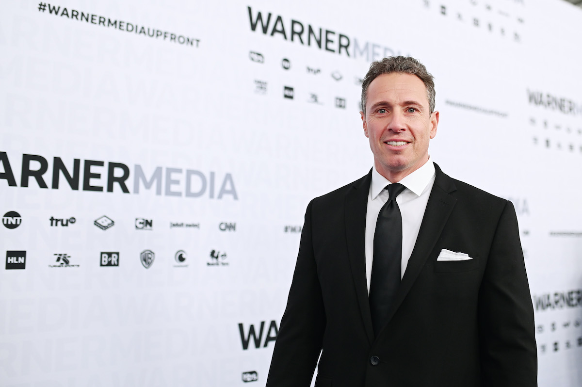 Chris Cuomo smiles awkwardly on a red carpet in front of a Warner Media backdrop.