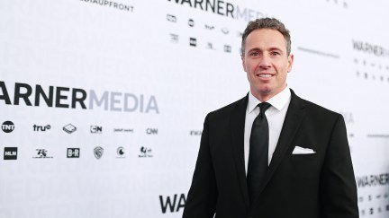 Chris Cuomo smiles awkwardly on a red carpet in front of a Warner Media backdrop.