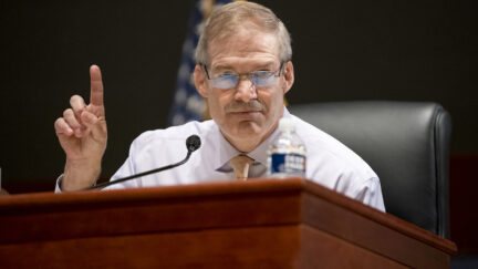 Jim Jordan looks into the camera and holds up a finger from his desk in the House.