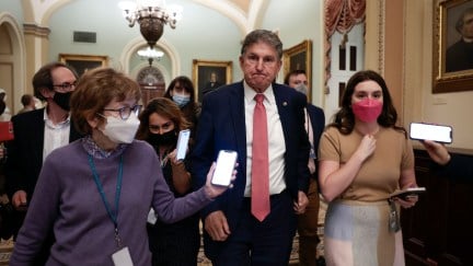 Joe Manchin frowns while walking with reporters in the Capitol