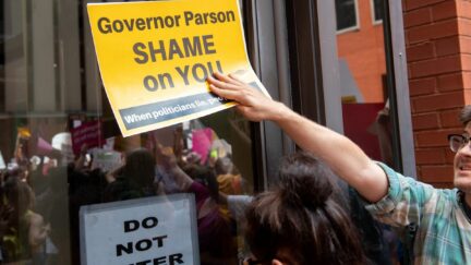 A protestor holds up a sign to a glass door reading 