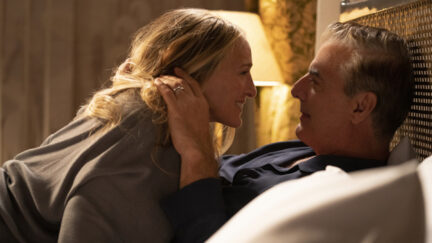 Carrie lies on top of Big in their bed and smiles at him.