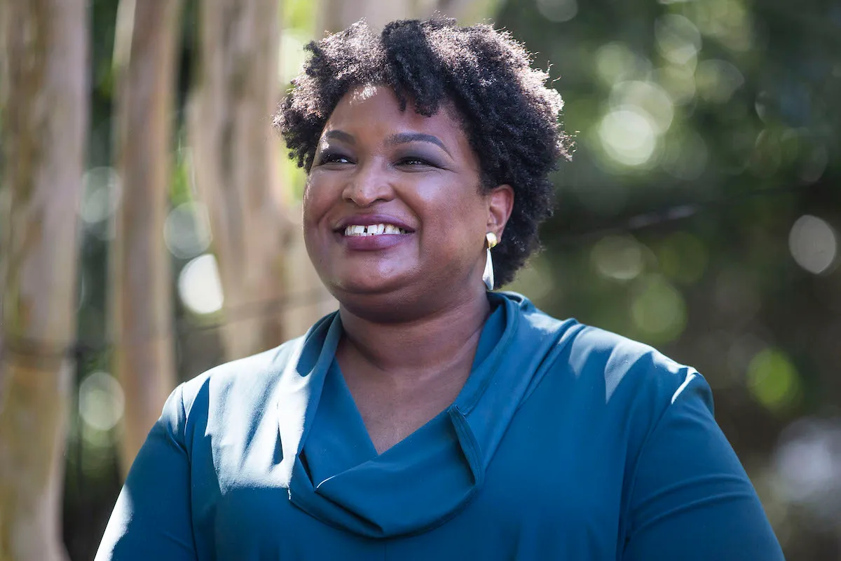 Stacey Abrams smiles against an outdoor background.