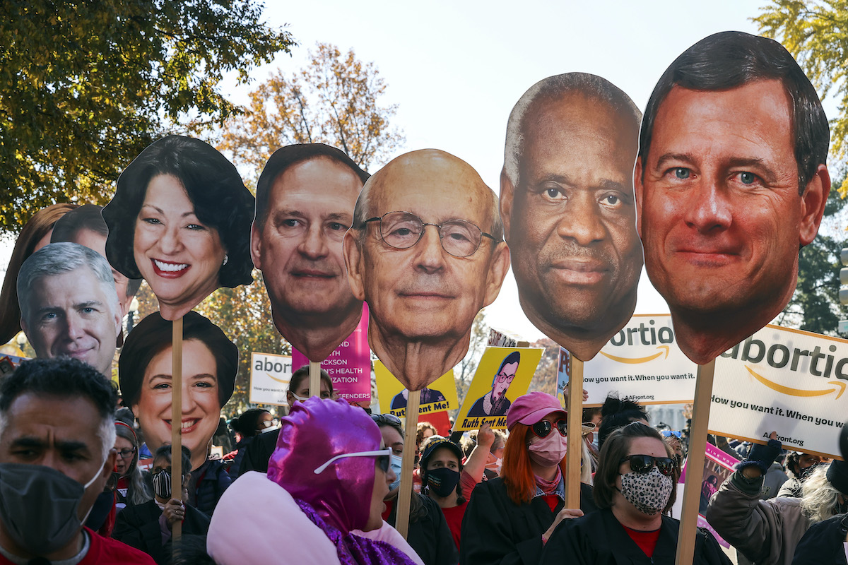 Activists hold giant photo cutouts of supreme court justices' faces during a protest