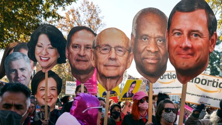Activists hold giant photo cutouts of supreme court justices' faces during a protest