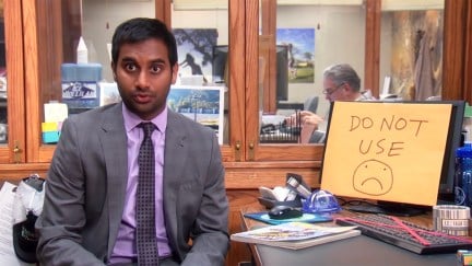 Tom Haverford sitting in front of a computer that says 