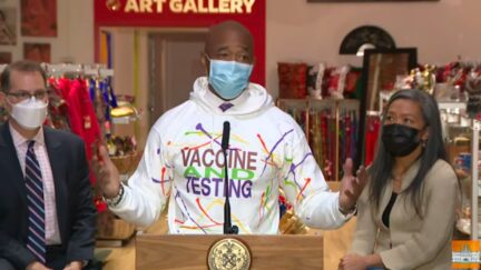 New York mayor Eric Adams gives a press conference in a white sweatshirt with a garish colorful logo for the covid-19 