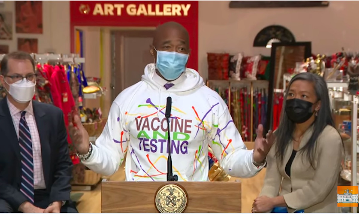 New York mayor Eric Adams gives a press conference in a white sweatshirt with a garish colorful logo for the covid-19 "vaccine and testing"