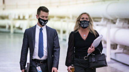 Marjorie Taylor Greene walks down a hallway in a mask reading 