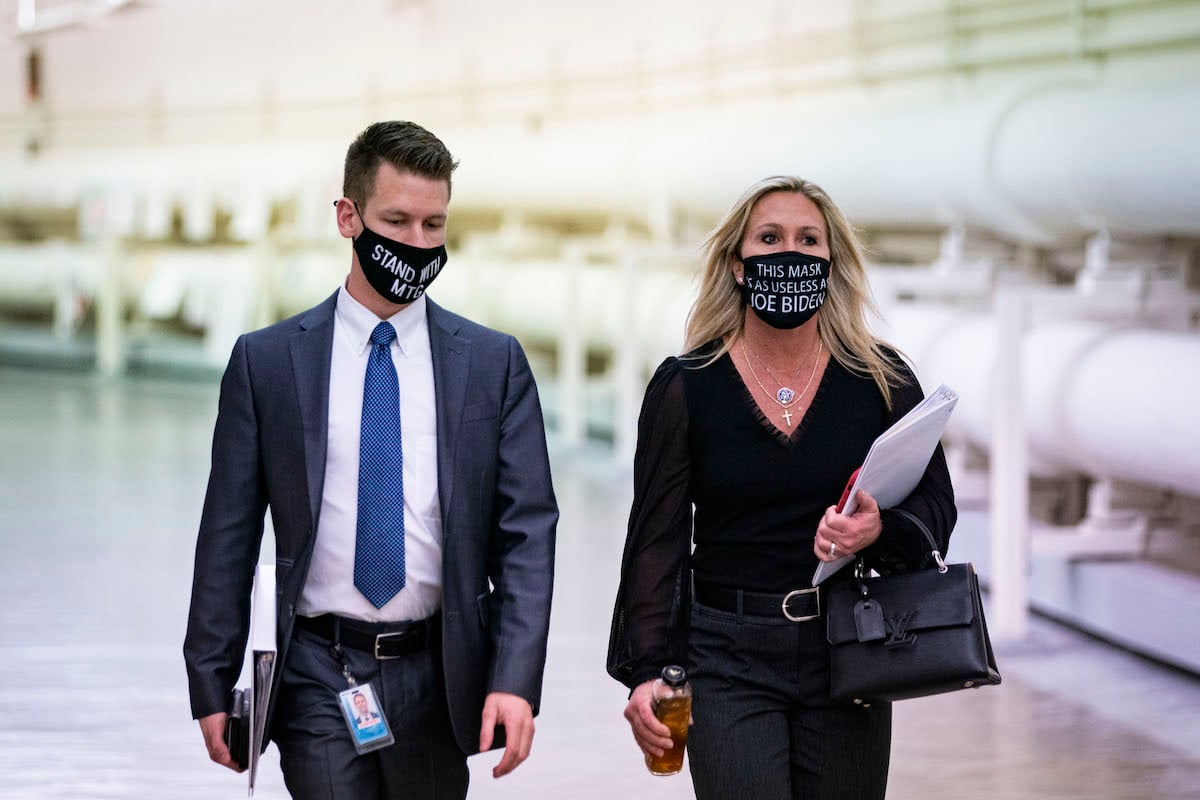 Marjorie Taylor Greene walks down a hallway in a mask reading "This mask is as useless as Joe Biden," next to a male staffer in a mask reading "stand with mtg"
