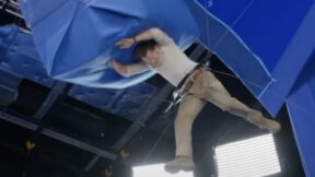 Tom Holland suspended in a harness while a giant blue box hits him in the head.