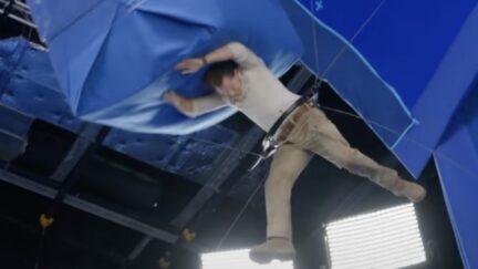 Tom Holland suspended in a harness while a giant blue box hits him in the head.