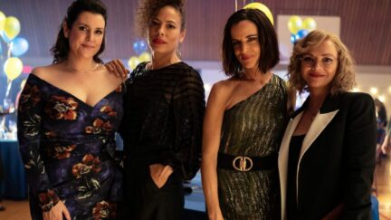 Four women stand side by side posing for a camera, wearing fancy dresses, in a scene from Yellowjackets