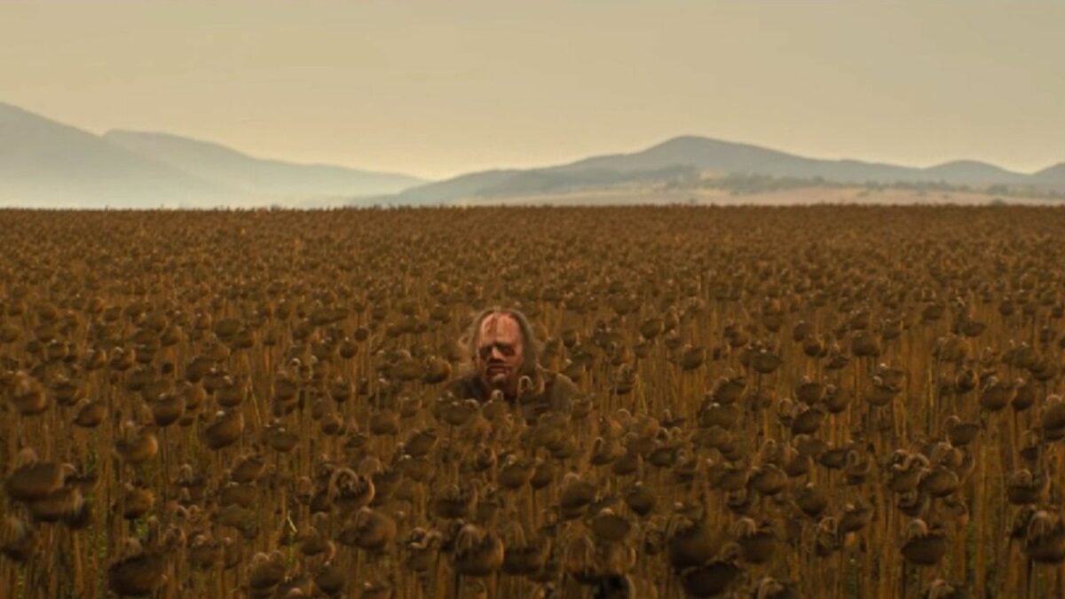Leatherface sitting in a field of sunflowers