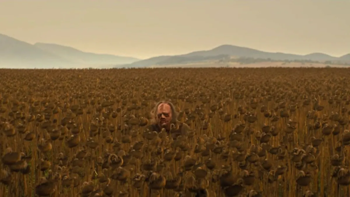Leatherface sitting in a field of sunflowers