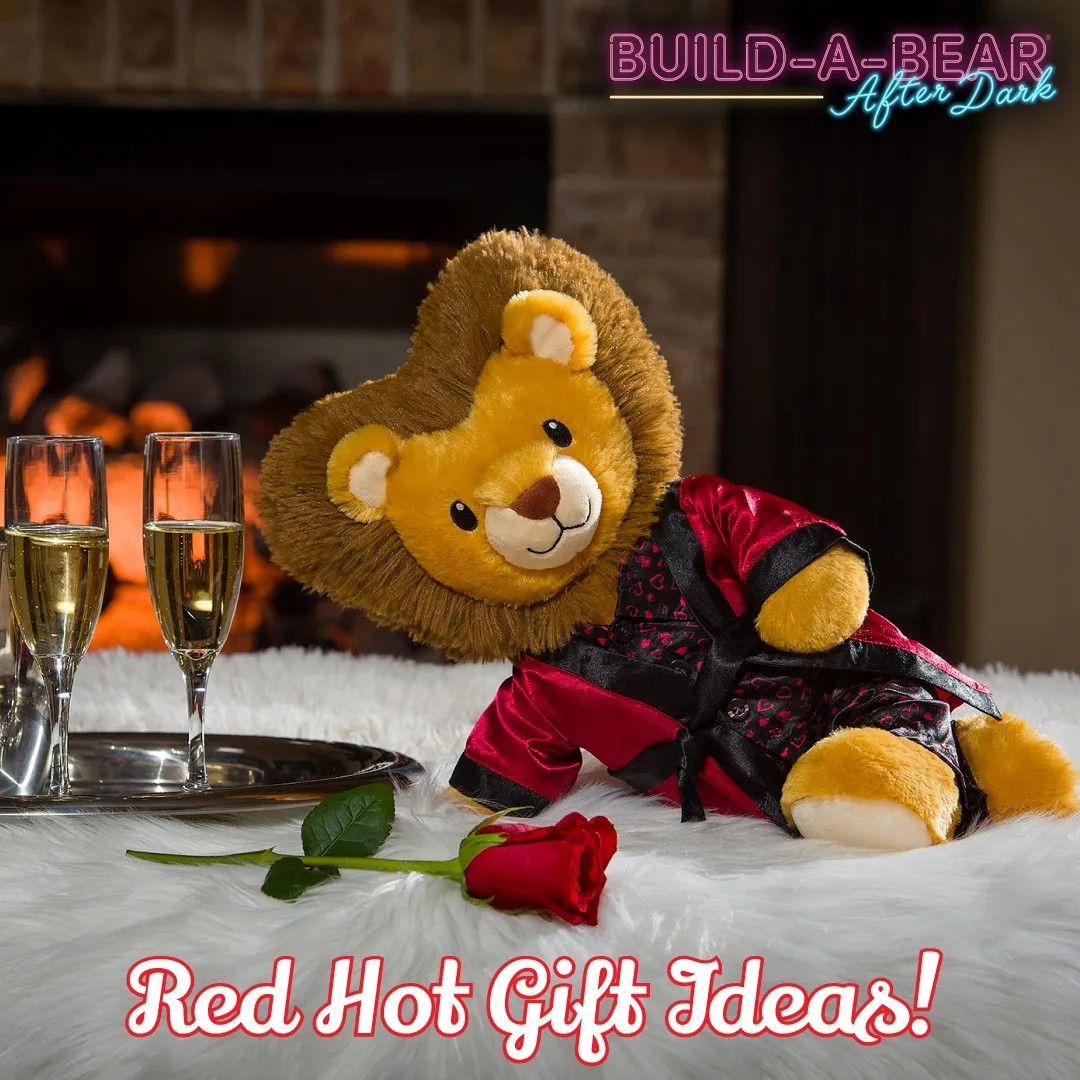 a stuffed lion in satin pajamas and robe is lounging suggestively next to glasses of champagne and a rose