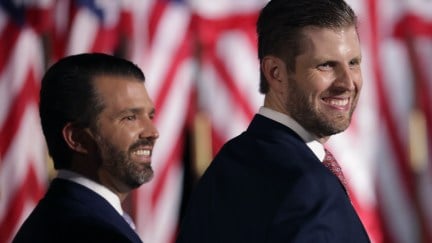 Donald Trump Jr. (L) and Eric Trump smile standing in front of an American flag.