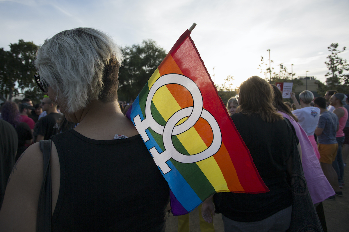 A person holds a rainbow flag with two female symbols on it
