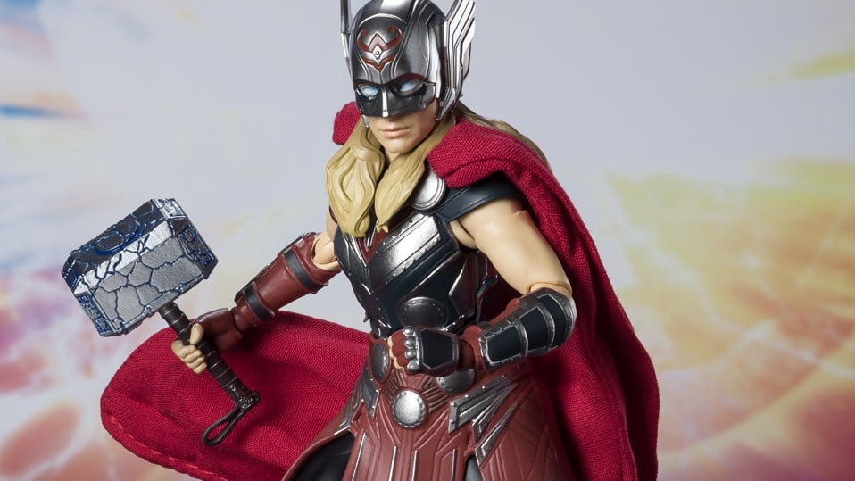 An action figure of Jane Foster as The Might Thor, wearing a helmet that covers her eyes and holding a version of Mjolnir covered in cracks.