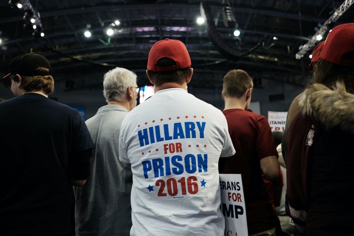 A Trump supporter sits in a crowd wearing a t-shirt reading "Hillary for Prison 2016" on the back