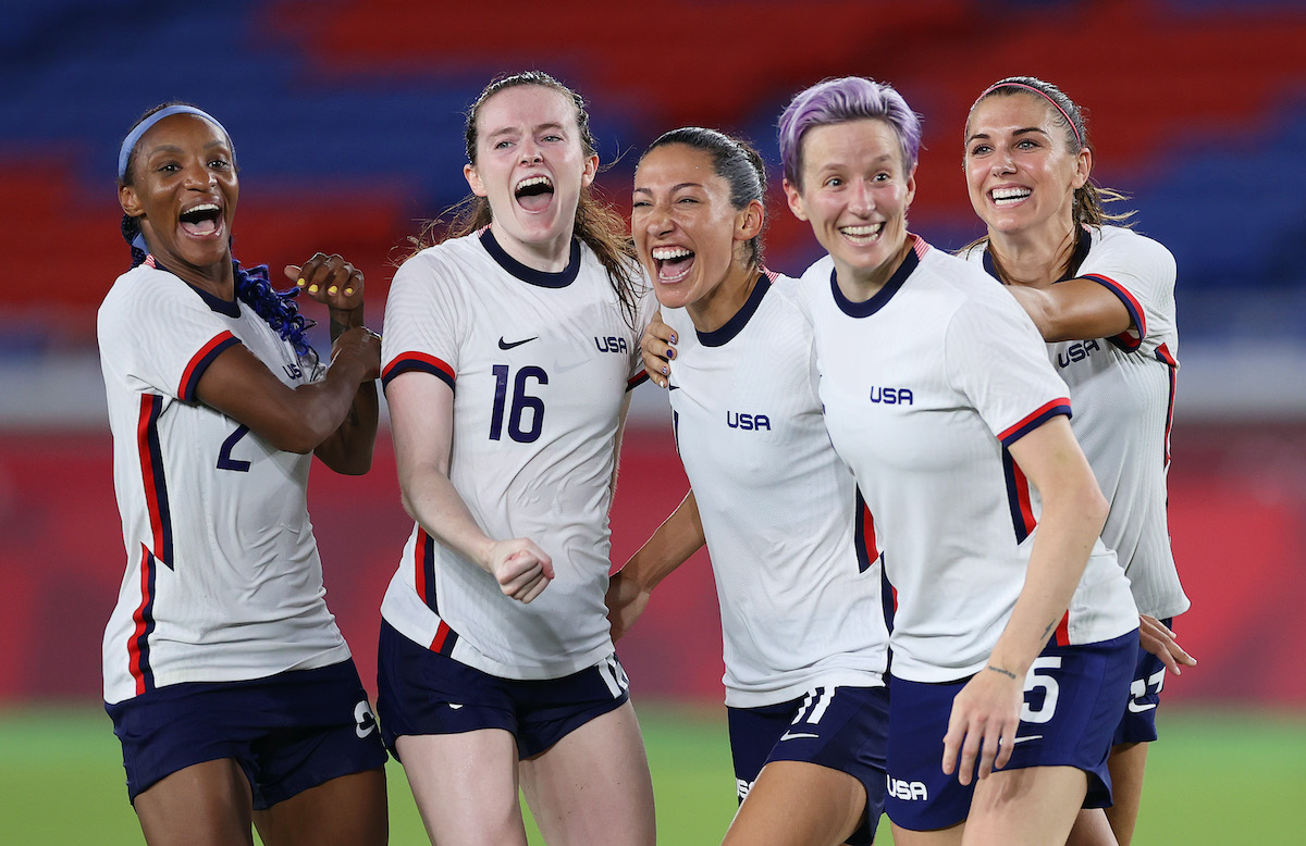 Members of the US Women's National Soccer Team smile and celebrate on the field.
