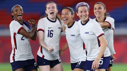 Members of the US Women's National Soccer Team smile and celebrate on the field.
