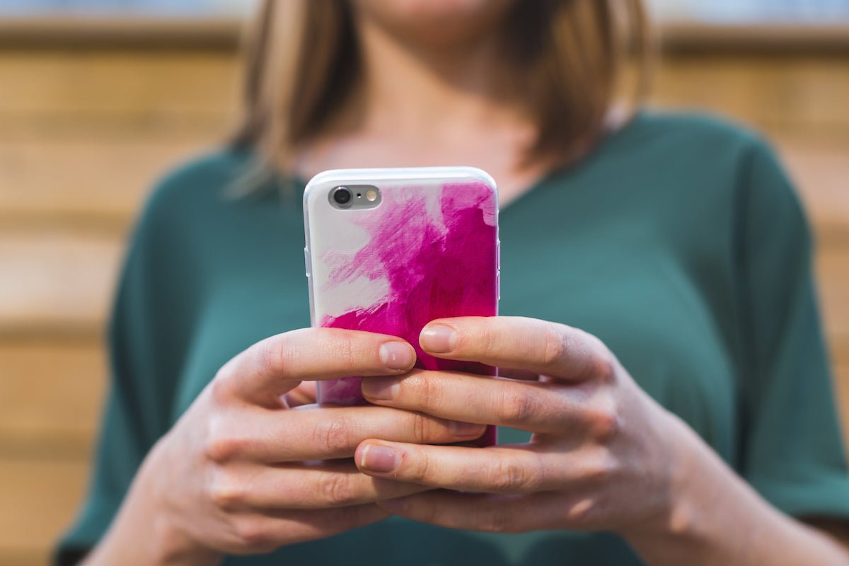 A white woman with her face obscured holds a cell phone in a pink case out in front of her