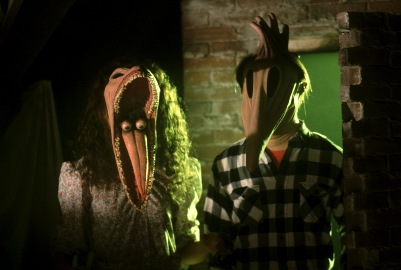 The Maitlands (Geena Davis and Alec Baldwin) distort their faces. Barbara Maitland has her jaw stretched out and her eyes on her tongue, and Adam has his face stretched out into a beak shape.