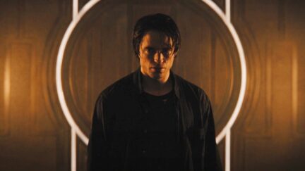Robert Pattinson as Bruce Wayne standing in front of a light
