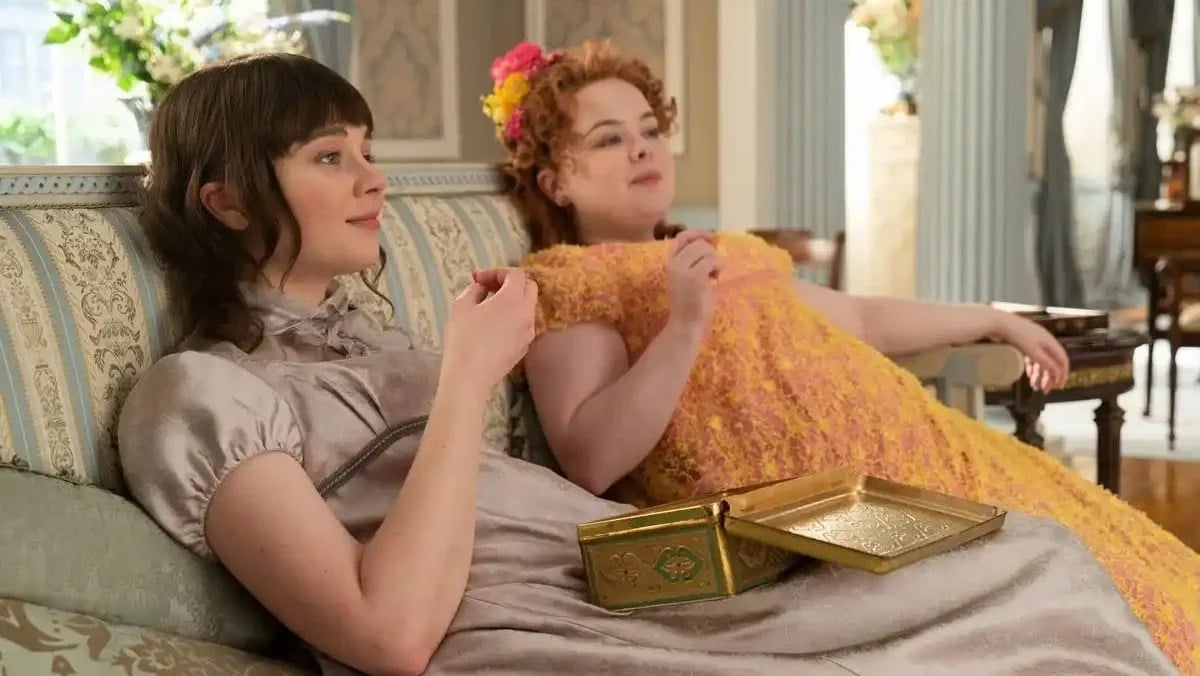 Penelope and Eloise of Bridgerton sit on a couch