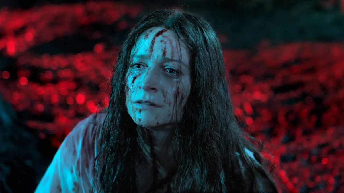 Enid Baines sits in a field covered in blood.