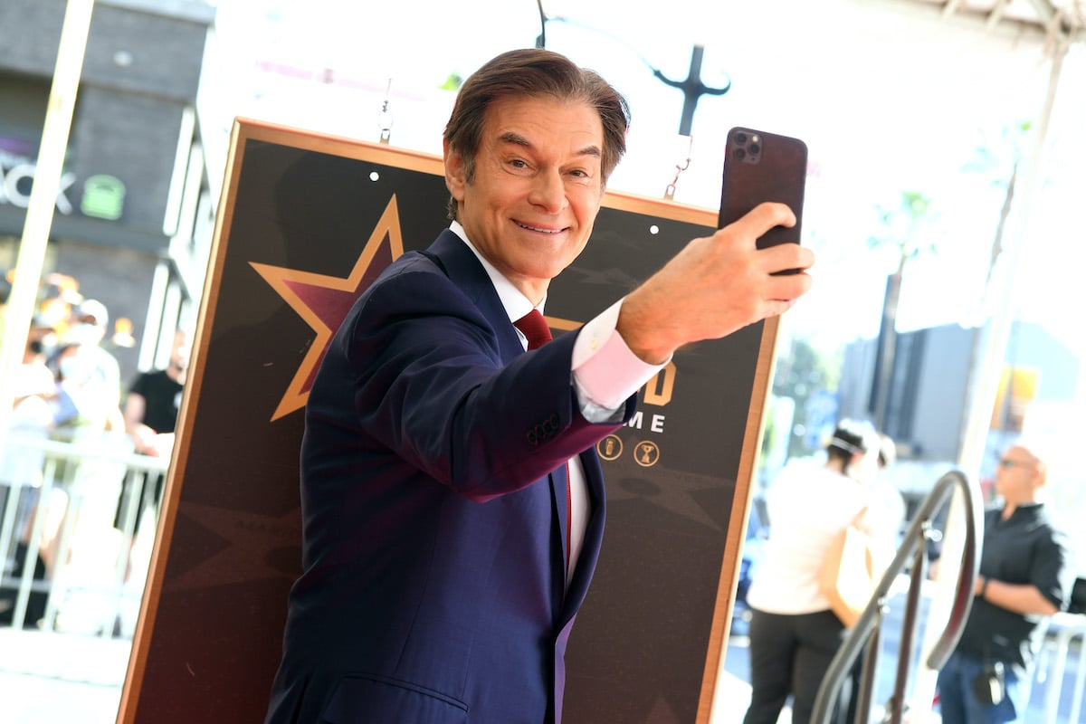 Dr Oz smiles at the camera as he holds his phone in front of himself to take a selfie.