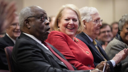 Clarence Thomas and Ginni Thomas laugh while seated in a crowd.