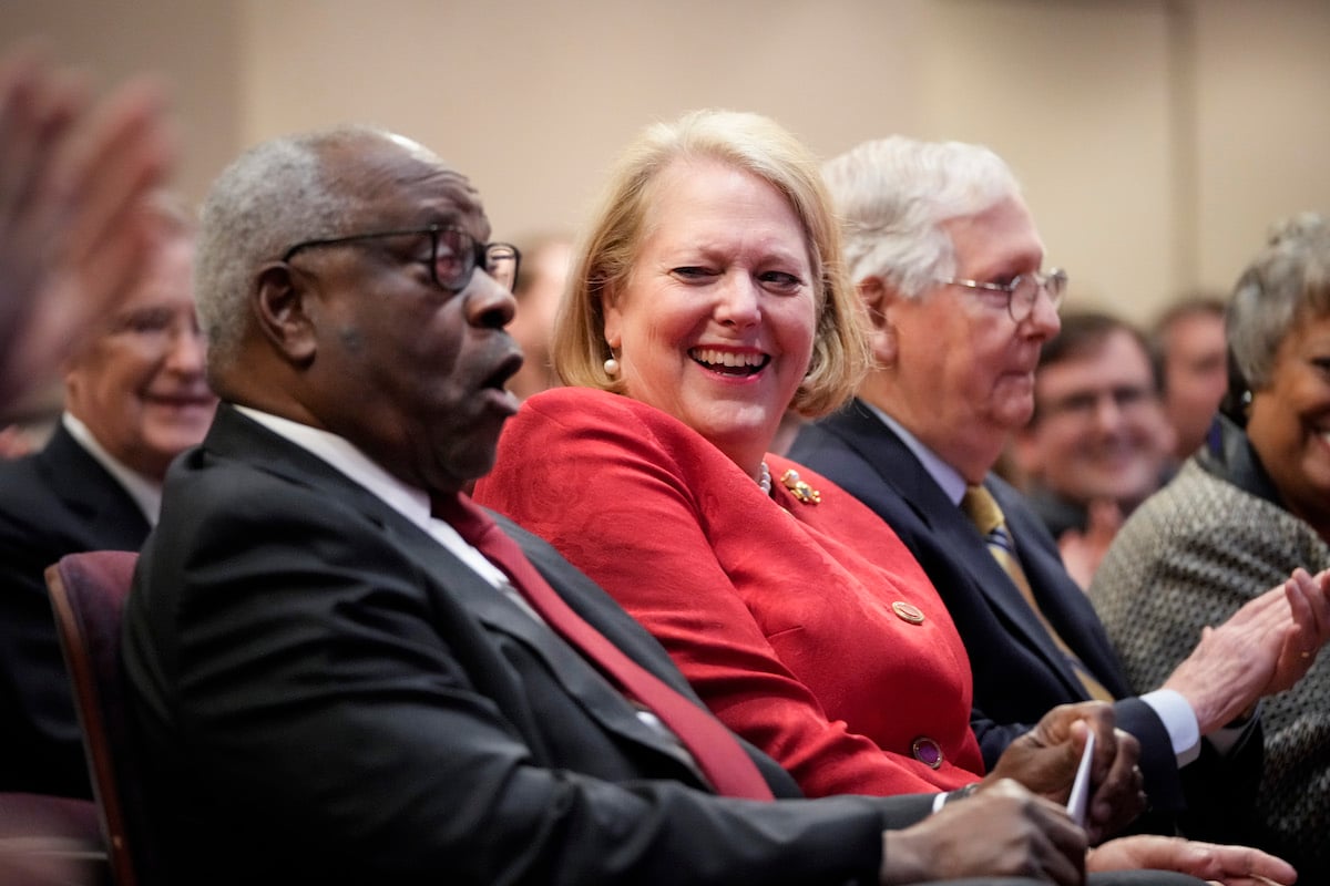 Clarence Thomas and Ginni Thomas laugh while seated in a crowd.